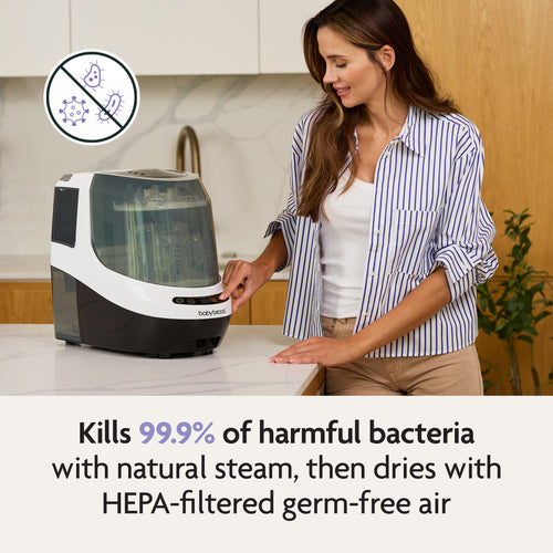 A woman uses the Baby Brezza UK Bottle Washer Pro - All In One Washer, Steriliser, Dryer in her kitchen. Text: Kills 99.9% of harmful bacteria with natural steam and dries with HEPA-filtered air. Bacteria icon appears top left. - product thumbnail