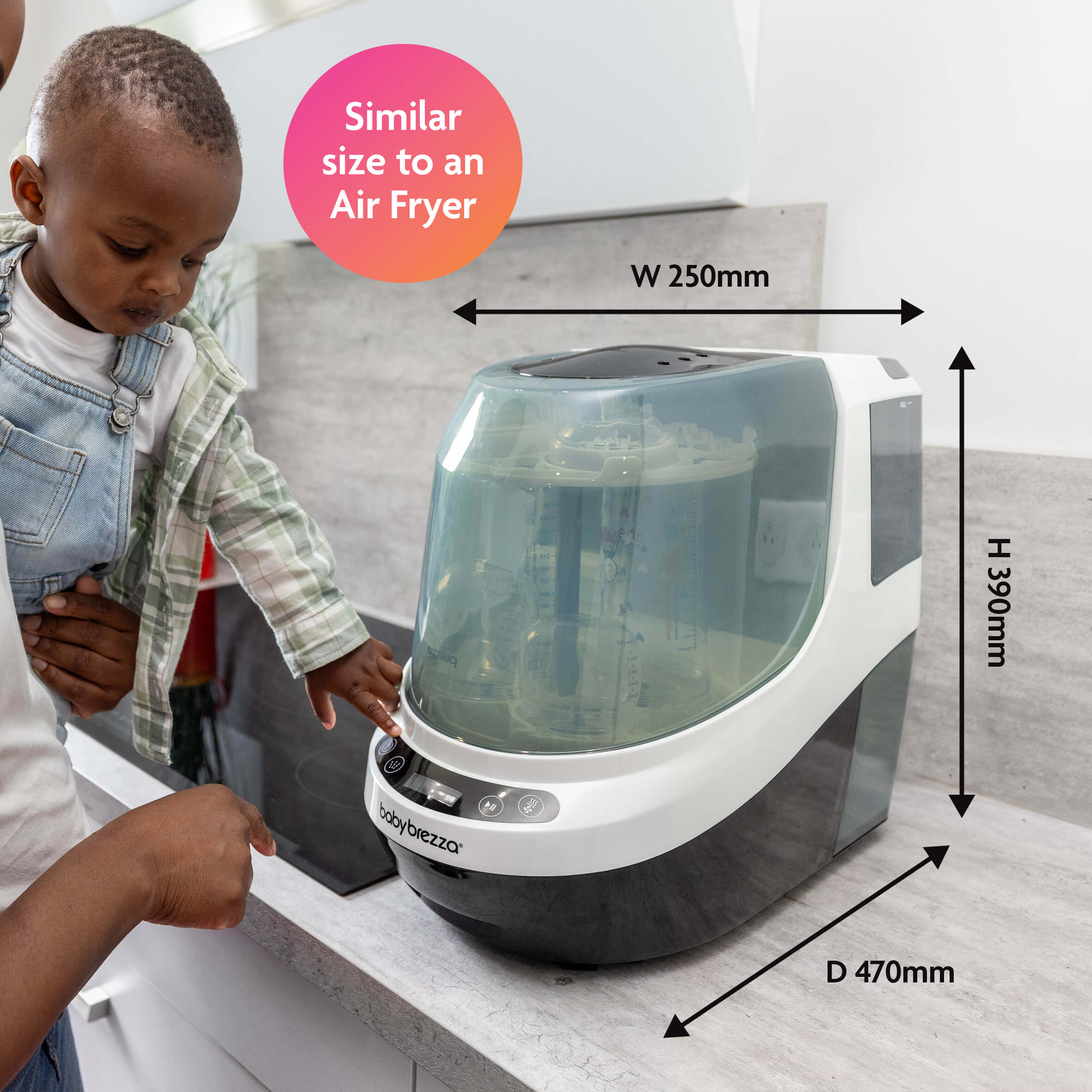 A woman holding a child points at the Baby Brezza UK BIG BREZZA BUNDLE - Formula Pro Advanced, Bottle Washer Pro + MUCH MORE! on a counter. Dimensions: W 250mm, H 390mm, D 470mm—similar in size to an air fryer. - product thumbnail