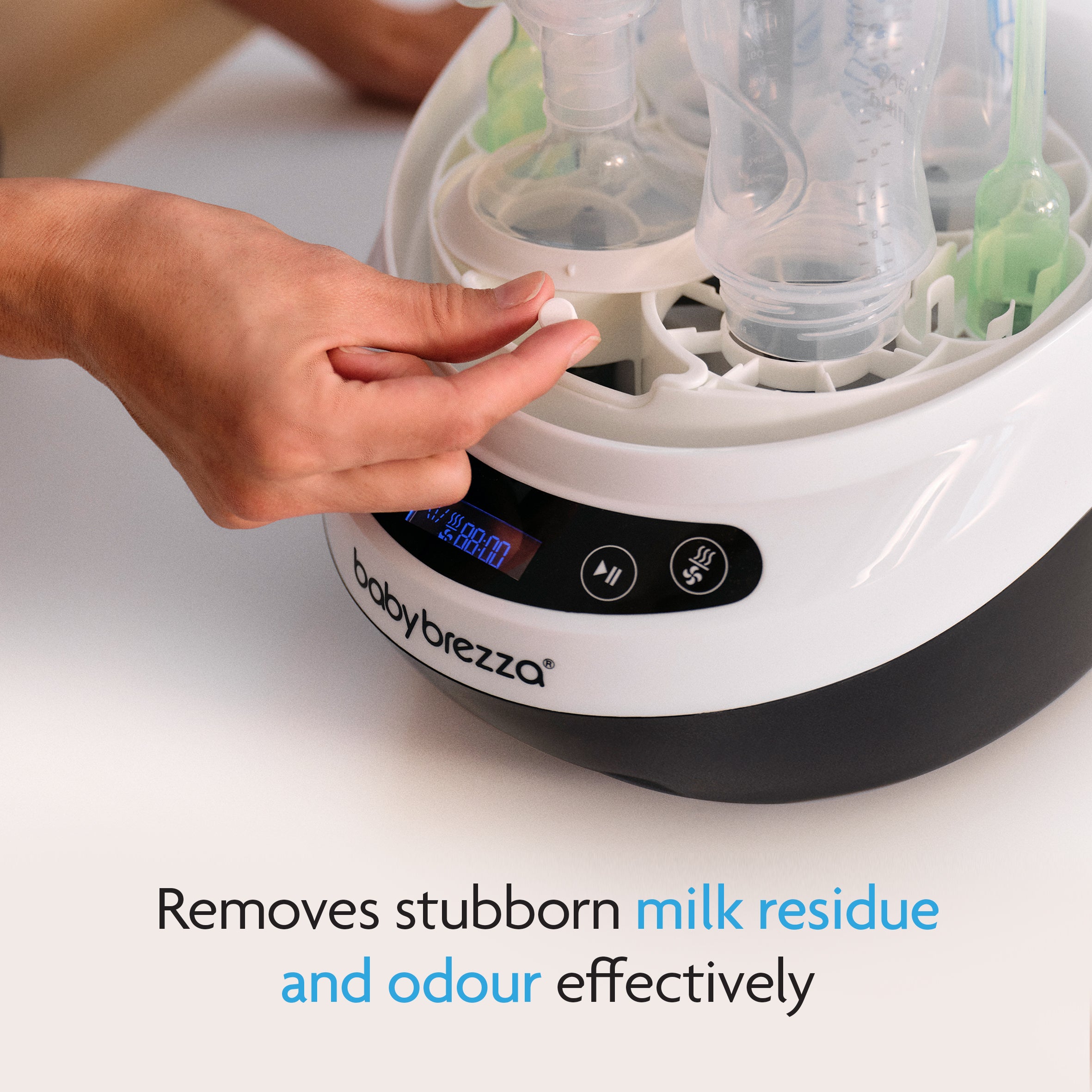 Close-up of a hand placing baby bottles into the Baby Brezza Bottle Washer Pro® with Detergent Tablets (120 count). The digital display is visible, and text below reads: Safely removes milk residue and odour with baby-safe cleaning. - product thumbnail