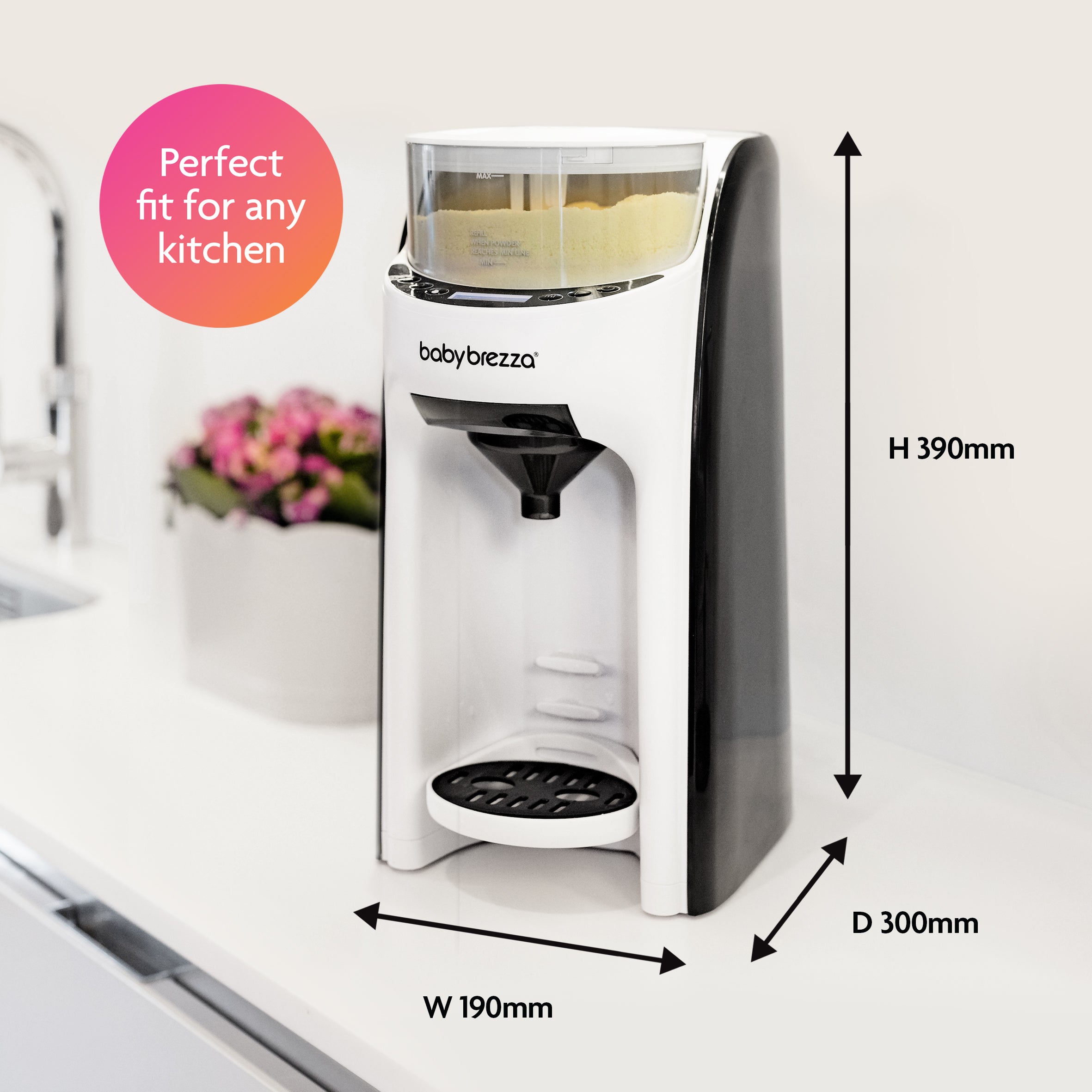 A black and white Baby Brezza UK BUNDLE: Formula Pro Advanced + Extra Funnel & Cover Set sits on a kitchen counter (390mm H x 190mm W x 300mm D). A pink circle says Perfect fit for any kitchen. Flowers are in the background. - product thumbnail