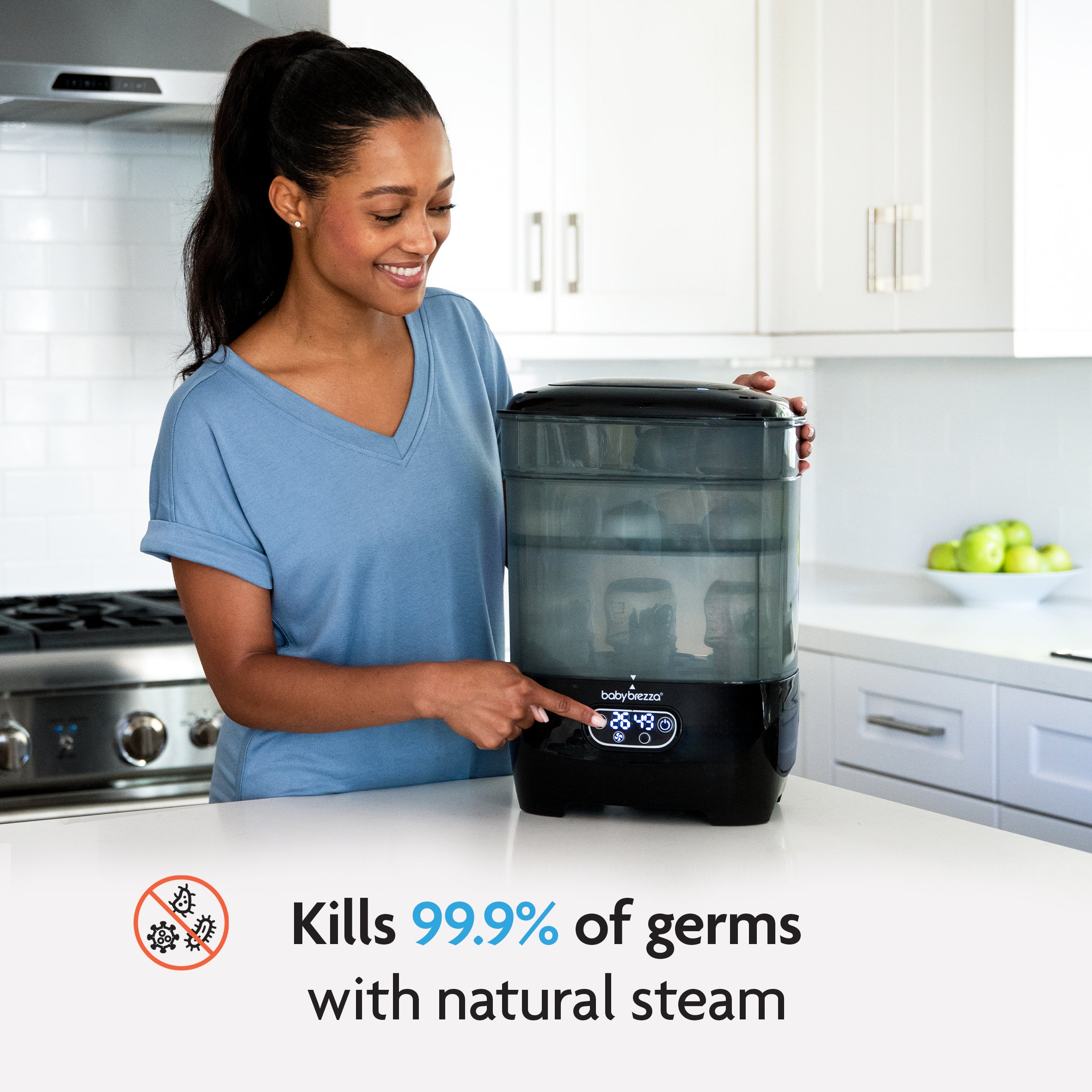 A smiling woman in a blue shirt uses the Baby Brezza UK Steriliser Dryer Advanced in a bright kitchen. Text reads: Kills 99.9% of germs with natural steam, next to a no-germs icon. - product thumbnail