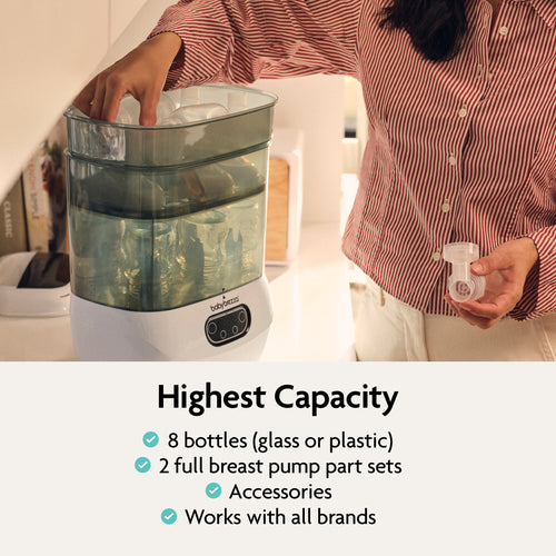A user loads items into the Baby Brezza UK BUNDLE Steriliser Dryer Advanced Black, which sterilises 8 bottles, 2 breast pump sets and accessories; plus a universal bottle warmer for all brands of milk and formula. - product thumbnail
