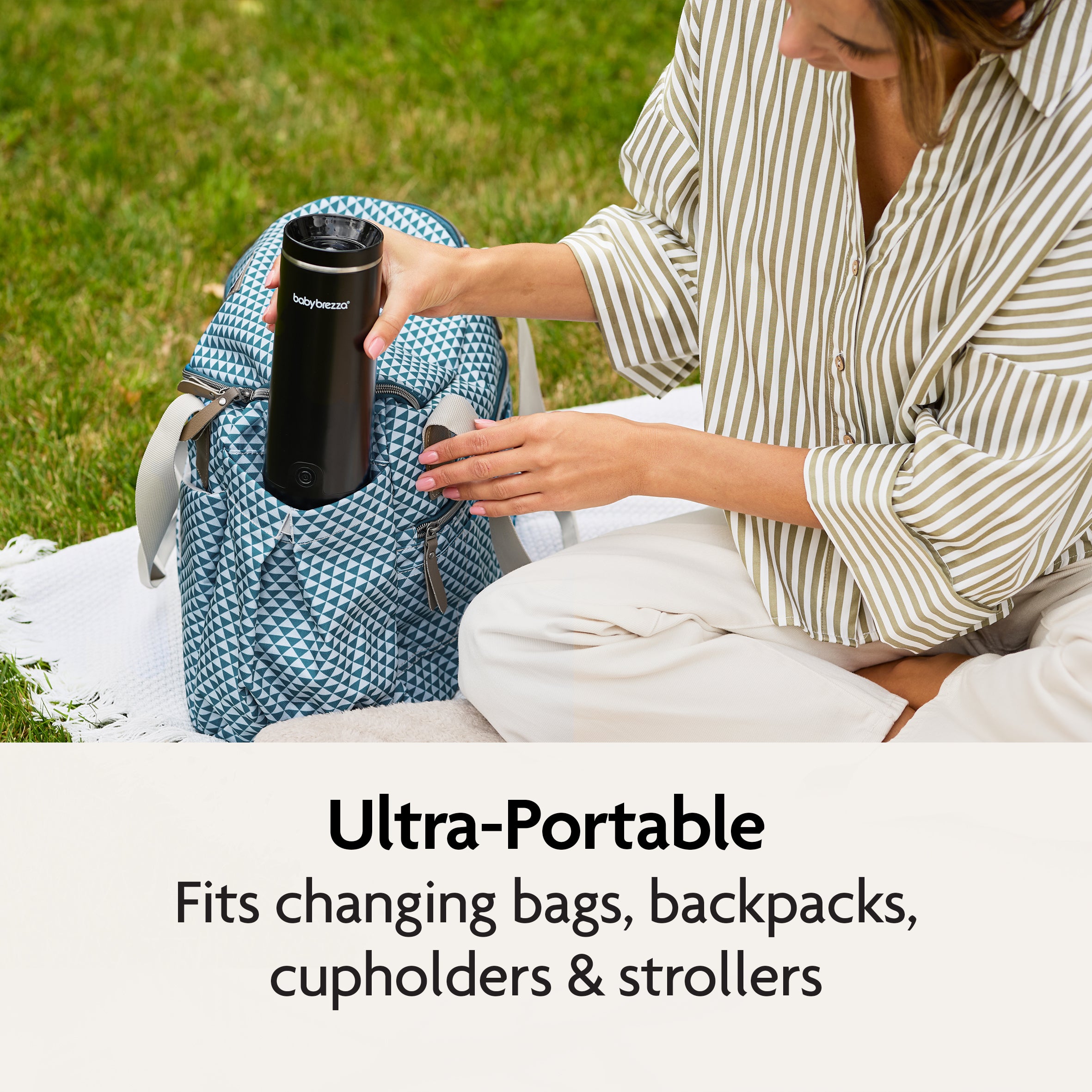 A woman sits on a blanket outdoors, placing the Baby Brezza UK SuperFast Portable Bottle Warmer into a patterned blue backpack. Text below reads: Ultra-portable—fits changing bags, backpacks, cupholders & strollers. - product thumbnail