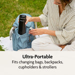 A woman sits on a blanket outdoors, placing the Baby Brezza UK SuperFast Portable Bottle Warmer into a patterned blue backpack. Text below reads: Ultra-portable—fits changing bags, backpacks, cupholders & strollers. - product thumbnail