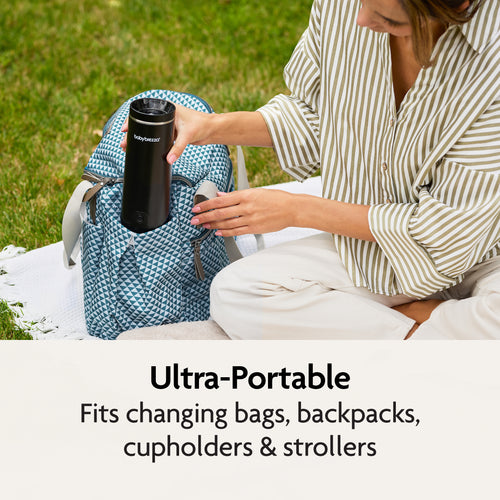 A woman sits on a blanket outdoors, placing the Baby Brezza UK SuperFast Portable Bottle Warmer into a patterned blue backpack. Text below reads: Ultra-portable—fits changing bags, backpacks, cupholders & strollers. - product thumbnail