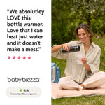 A woman smiles outdoors on a blanket, pouring hot water from the Baby Brezza UK SuperFast Portable Bottle Warmer into a baby bottle. Next to her sits a blue diaper bag and a positive review for the bottle warmer. - product thumbnail