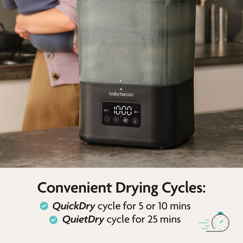 A person stands by a kitchen counter with the Baby Brezza BUNDLE Formula Pro Advanced And SuperQuick Steriliser - All Black, displaying 10:00 on its screen. Text highlights QuickDry (5/10 min) and QuietDry (25 min) cycles. Brand: Baby Brezza UK. - product thumbnail