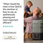 A smiling woman holds a toddler in the kitchen beside the Baby Brezza UK BUNDLE Formula Pro Mini White and SuperQuick Steriliser Black. A review praises its speed, ease, and efficiency with a 4.4 rating and five stars shown below. - product thumbnail