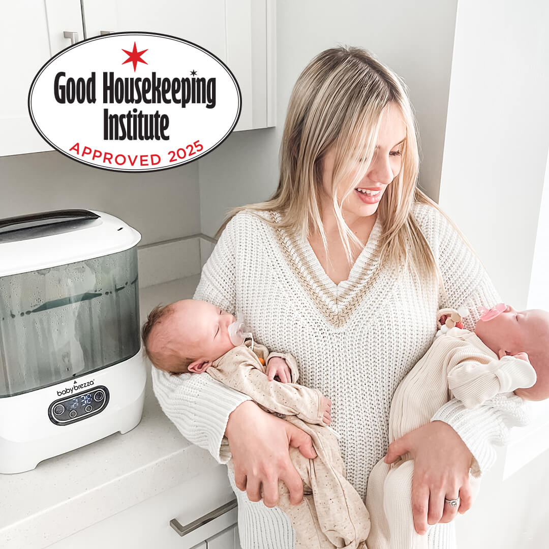 A smiling woman in a white sweater stands in a bright kitchen holding two newborns. The Steriliser Dryer Advanced sits on the counter beside her. A “Good Housekeeping Institute Approved 2025” badge is in the top left corner. - product thumbnail