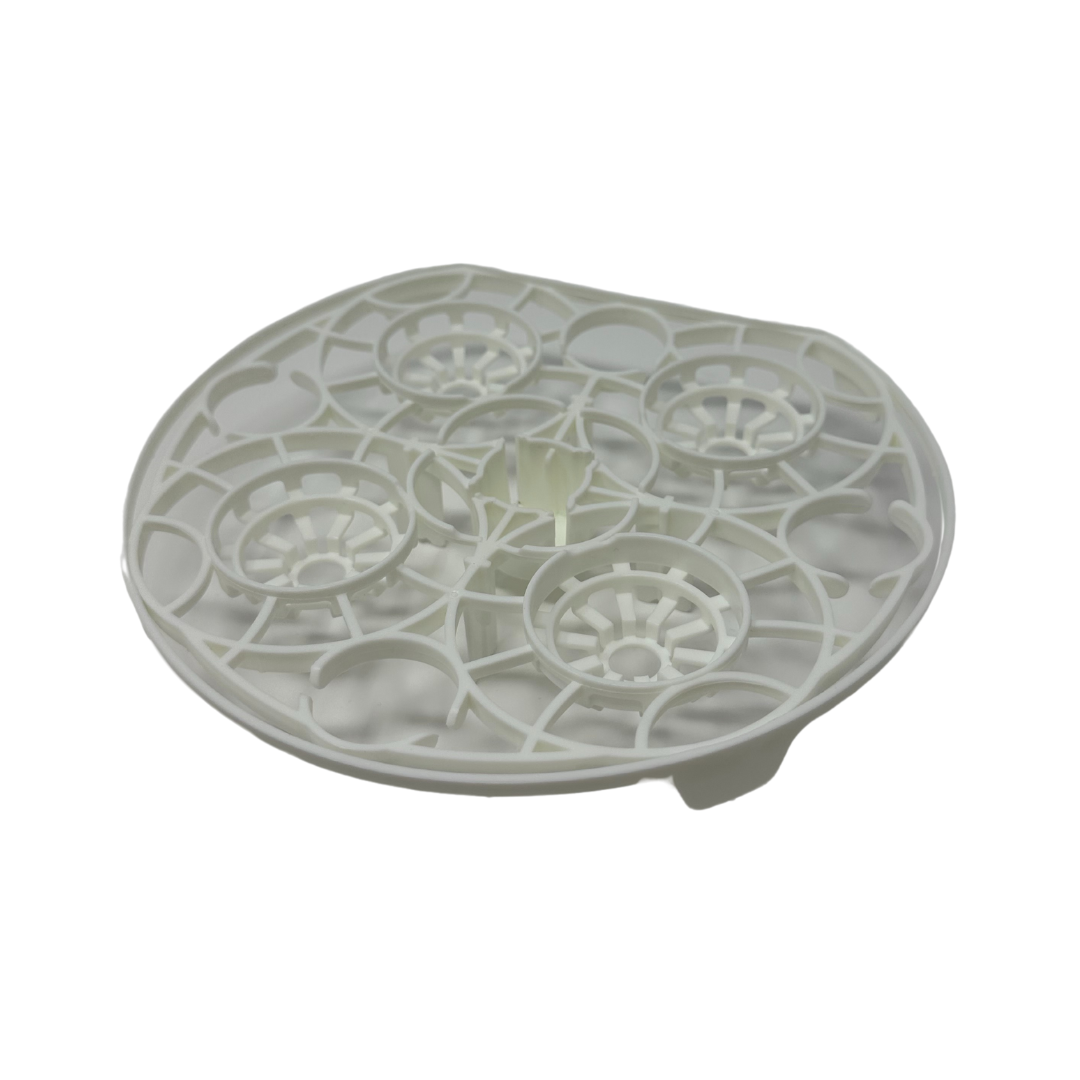 The Baby Brezza UK Bottle Washer Replacement Top Rack is a round, white plastic part with four raised circles and a grid pattern, designed for use in your dishwasher’s top rack, shown on a white background. - product thumbnail