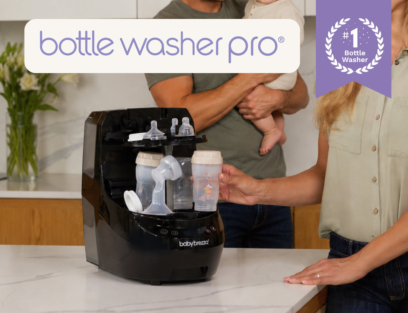 A Baby Brezza bottle washer pro on a kitchen counter with a woman standing beside it and a baby being held in the background. A purple badge in the top left says 'number 1 bottle washer' and a white banner at the top reads 'bottle washer pro'.