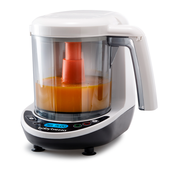 A white and black Baby Brezza baby food maker with an orange puree inside, shown on a white background. The digital display and control buttons are visible on the front panel.